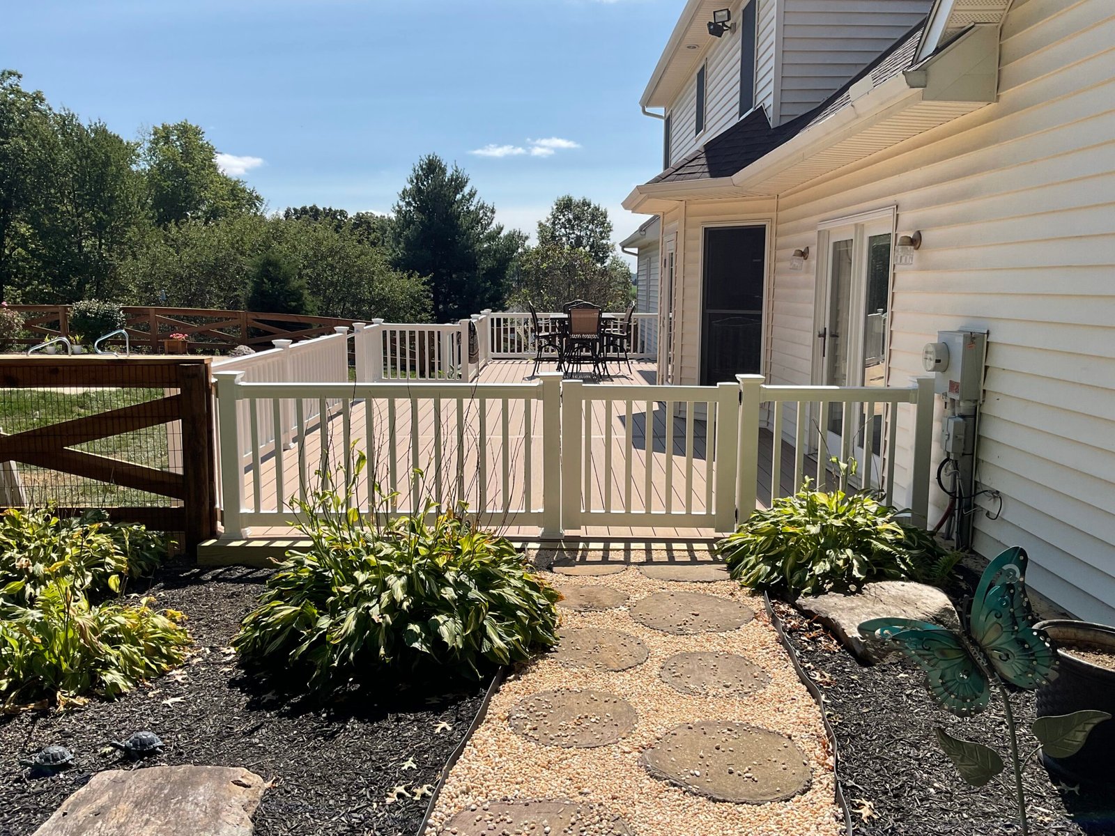 Backyard with white gate and stepping stones - Skyline Exteriors - Skyline Exteriors Backyard with white fence gate and stepping-stone path beside a beige home
