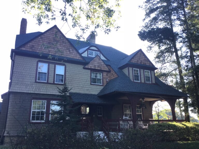 Two-story cedar-shingle home with new dark asphalt roof on a wooded lot