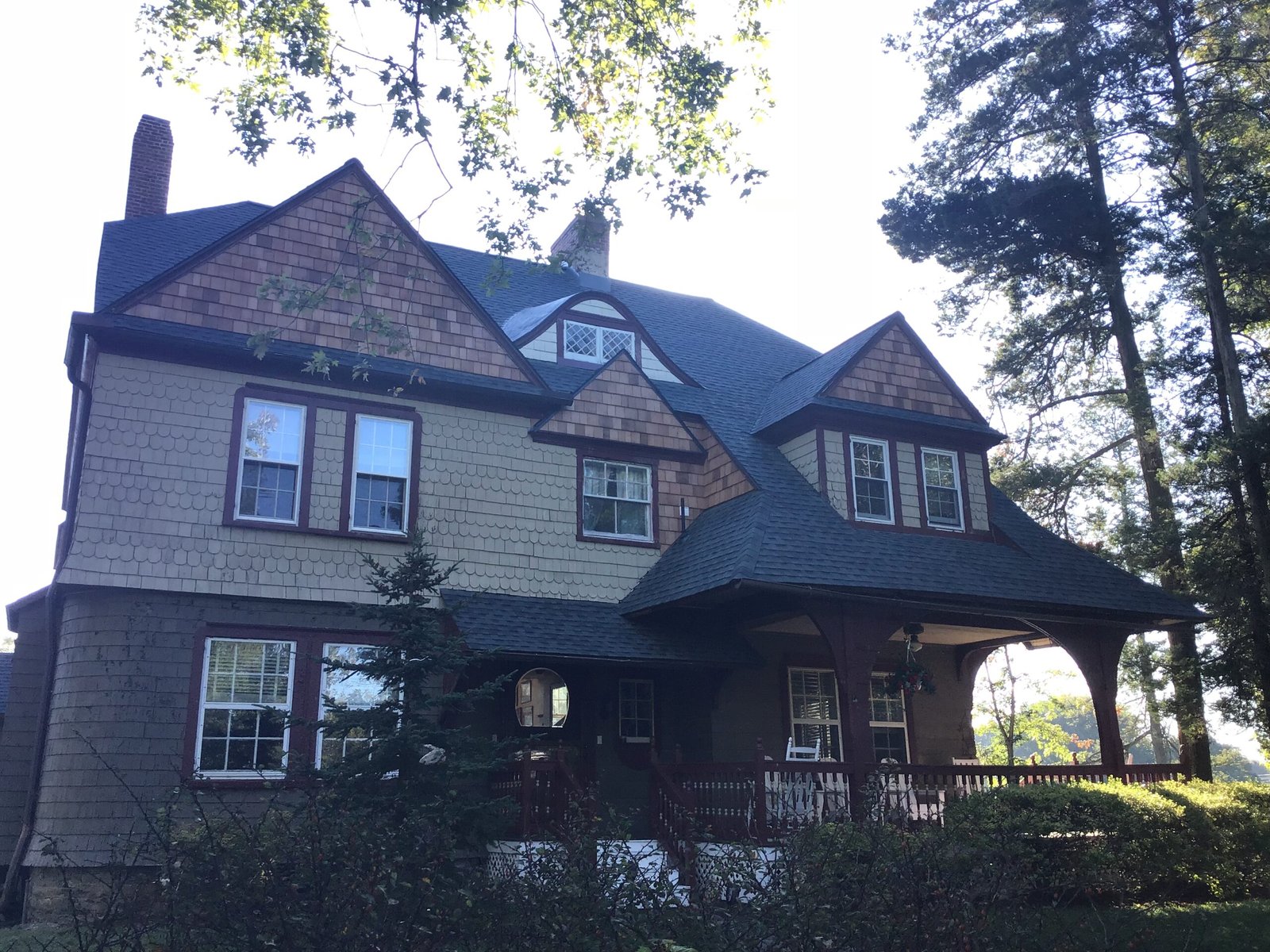 Two-story cedar-shingle home with new dark asphalt roof on a wooded lot
