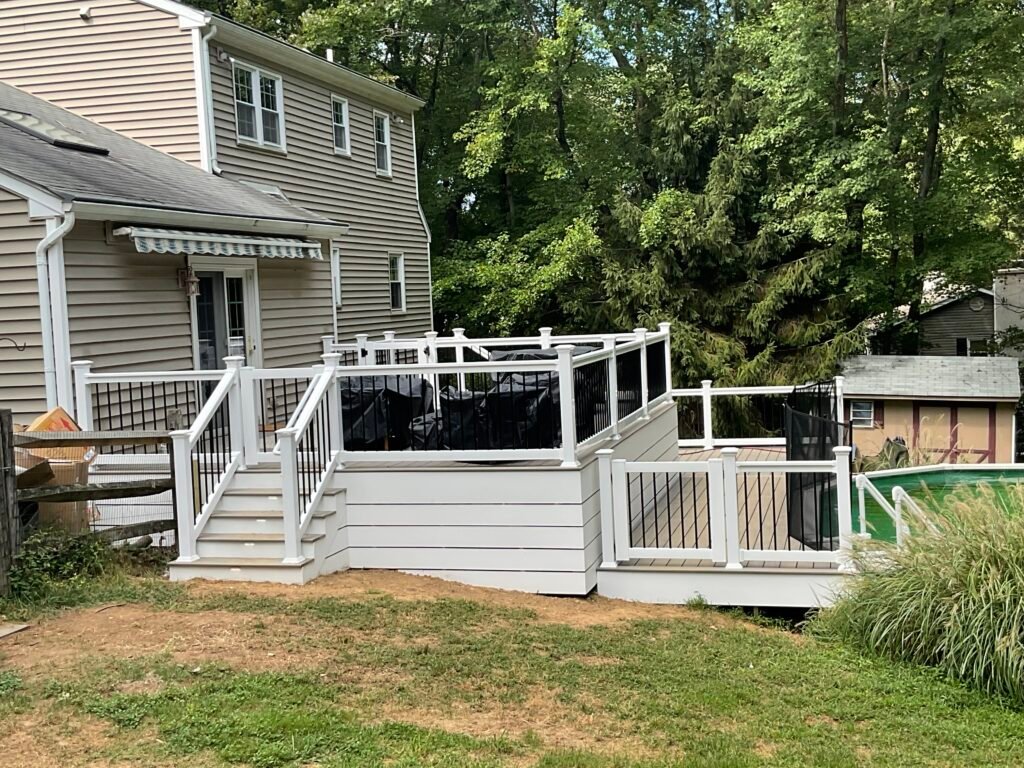 Multi-level composite deck with white railings - Skyline Exteriors - Skyline Exteriors Multi-level composite deck with white railings behind a gray two-story home