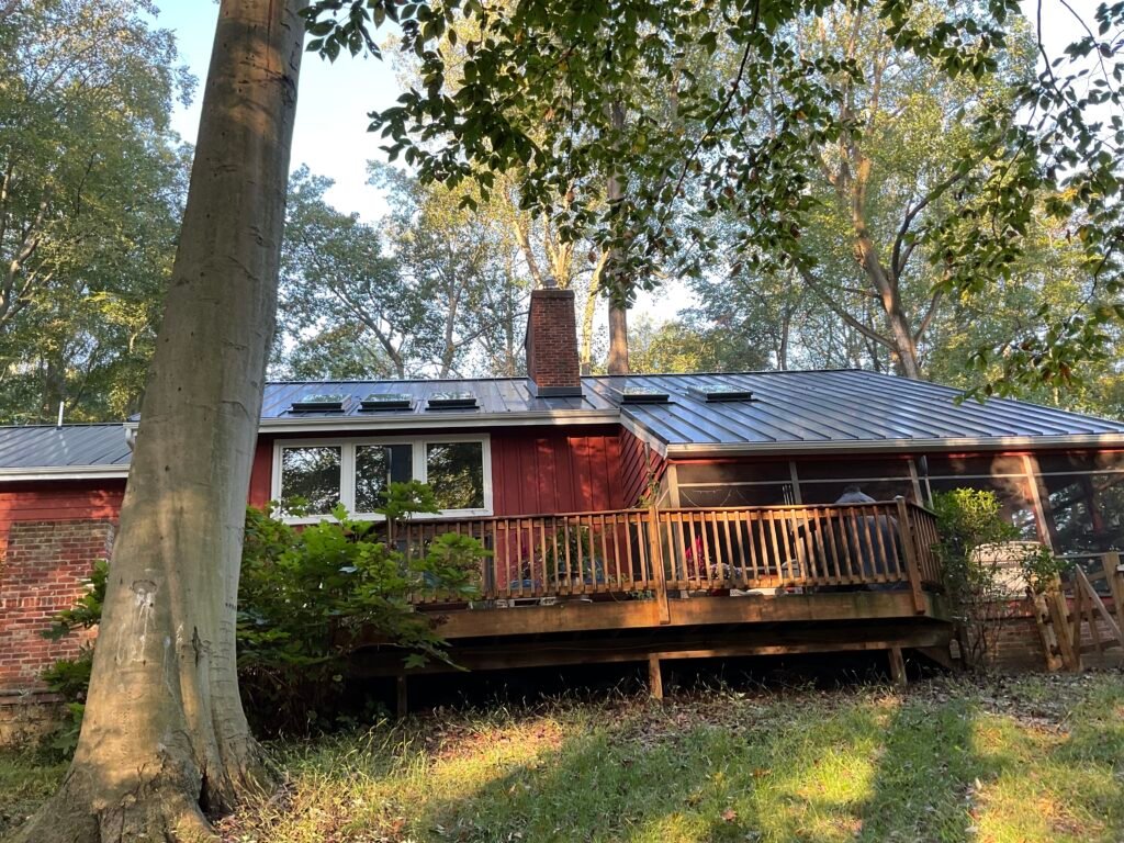 Red wood-sided home with metal roof and elevated wood deck among trees