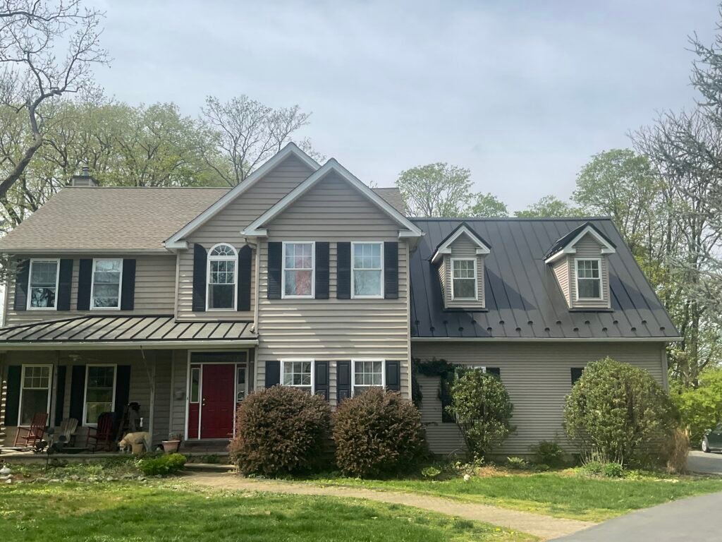 Standing-seam metal roof on a beige two-story home - Skyline Exteriors - Skyline Exteriors Beige two-story home with standing-seam metal roof, dormers and red front door