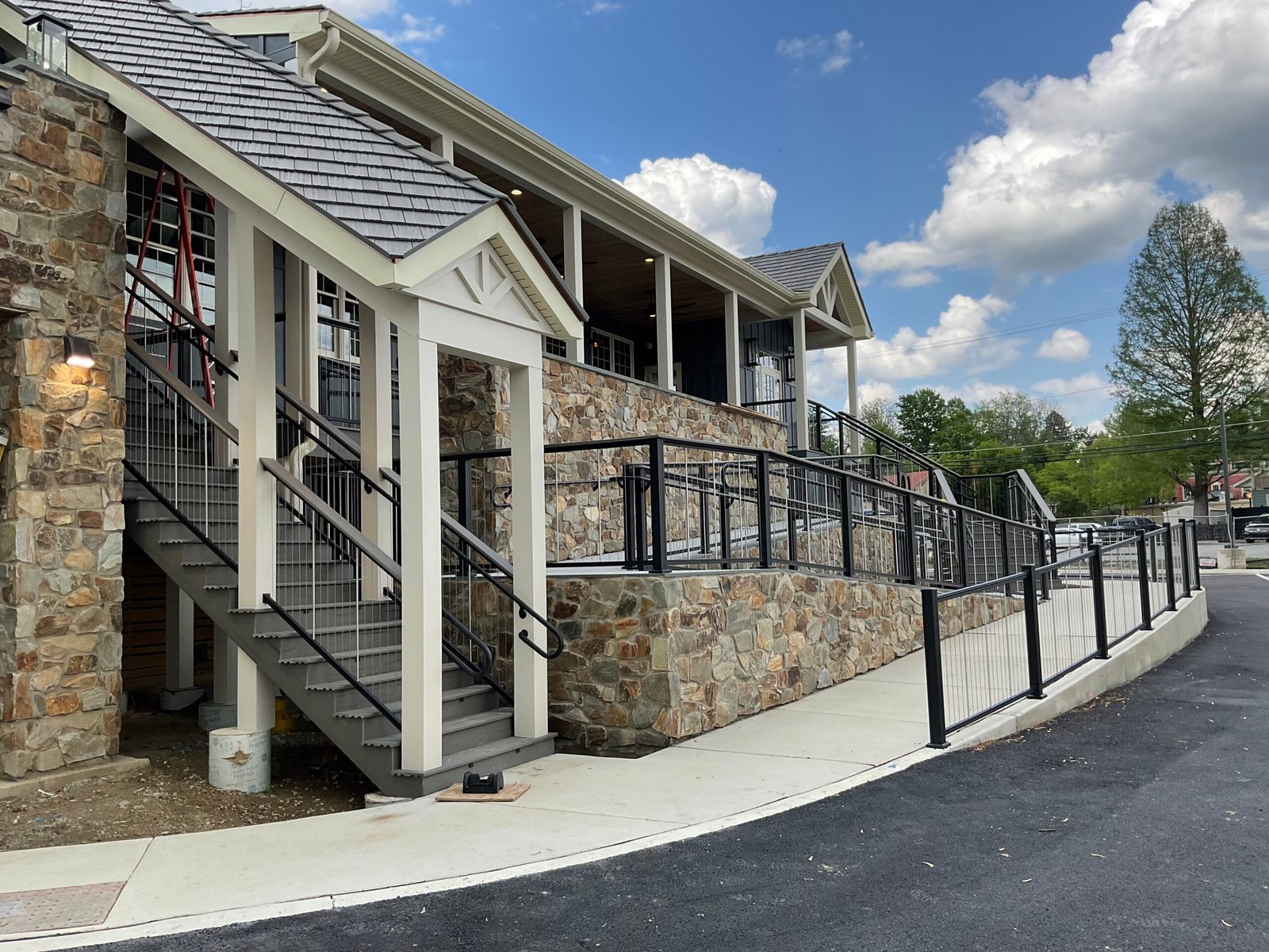 Stone-clad building with driveway railing - Skyline Exteriors - Skyline Exteriors Stone-clad building with white trim and black railing along the driveway