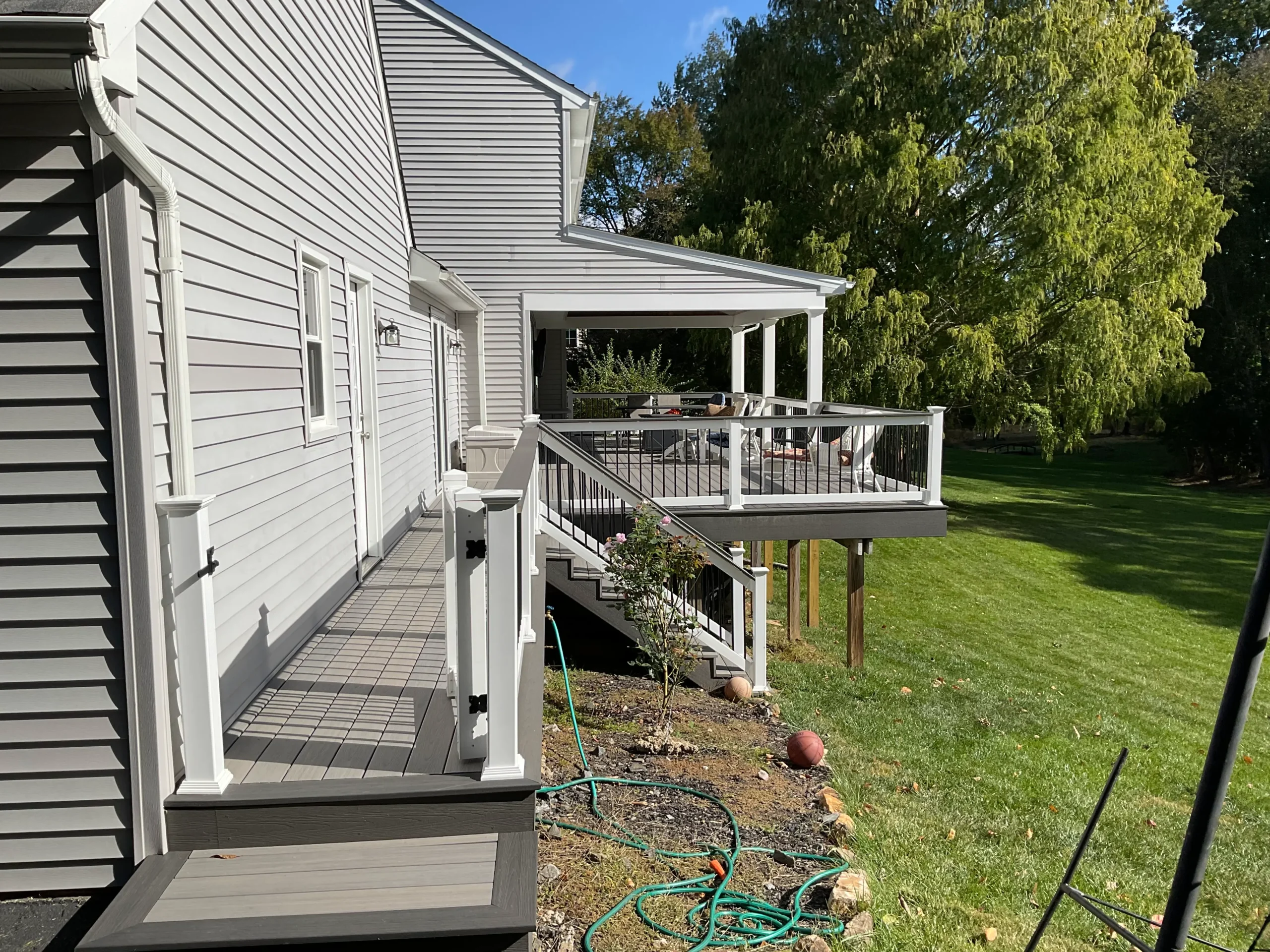 macungie-exterior-renovation - Skyline Exteriors - Skyline Exteriors Side view of a gray house with white trim and a multi-level deck with seating and railing, overlooking a green lawn.