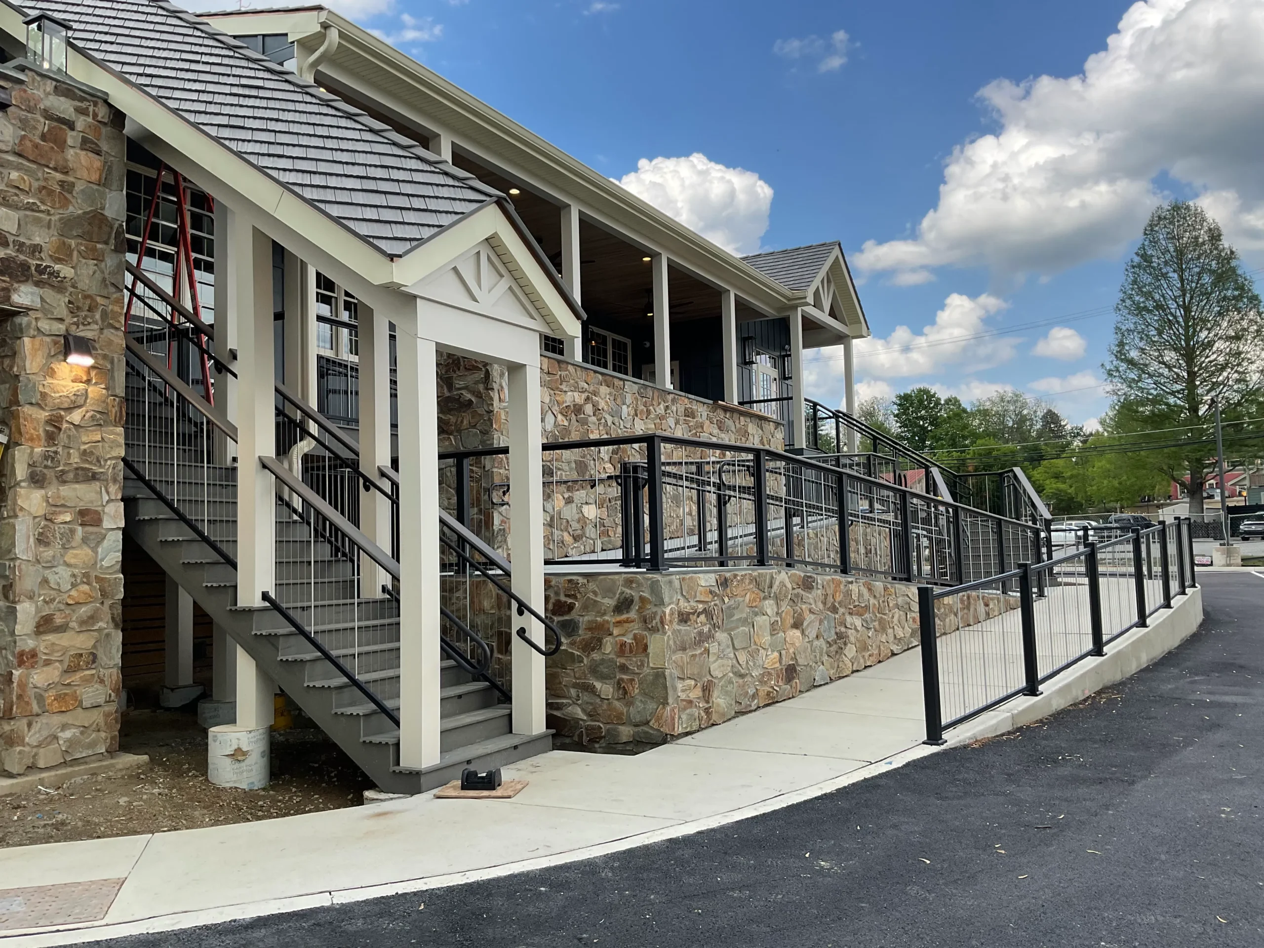 pa-home-exterior-upgrade - Skyline Exteriors - Skyline Exteriors Exterior view of a stone-clad building with cream trim, metal staircases, and black railings along a walkway under a blue sky with clouds.