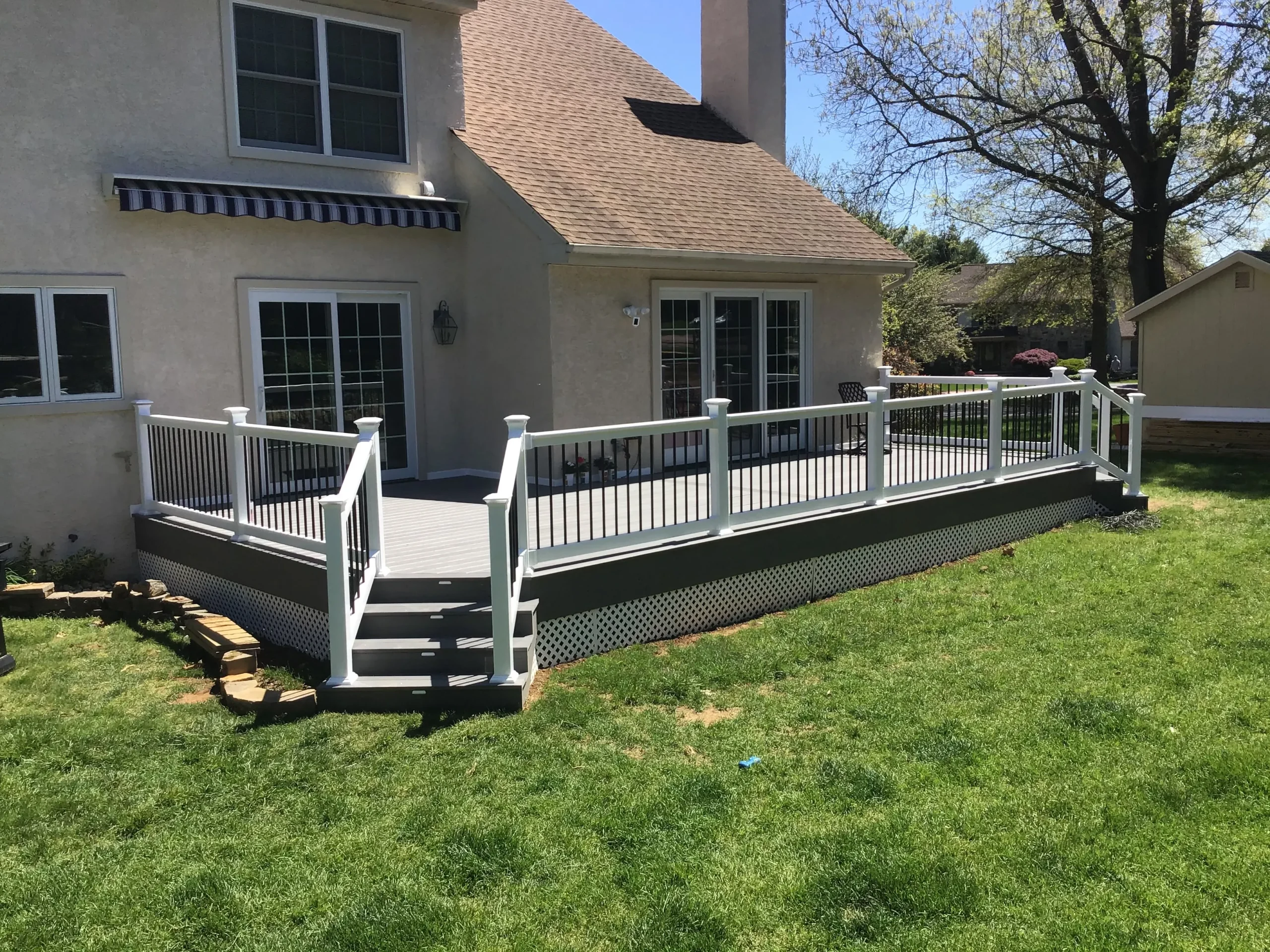 Backyard view of a beige stucco house with a raised white railing deck and sliding glass doors, on a sunny day.