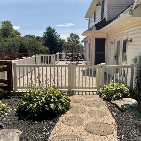 Backyard with white fence gate and stepping-stone path beside a beige home