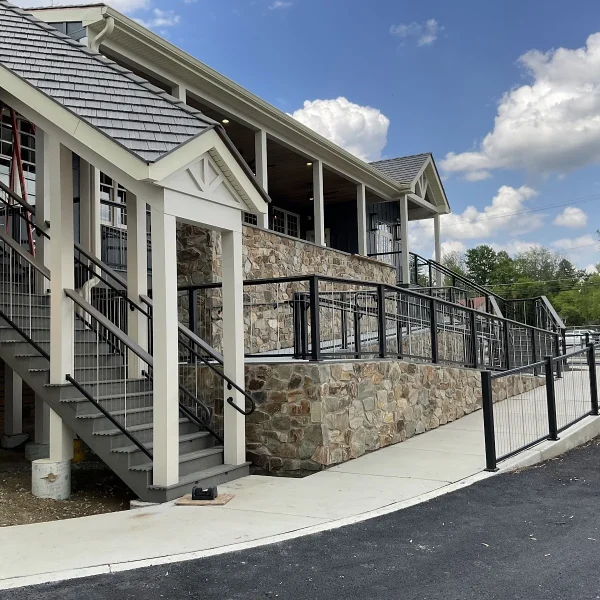 Exterior of a multilevel building with stone walls, white trim, and metal railings along stairs and a ramp under a blue sky with clouds.