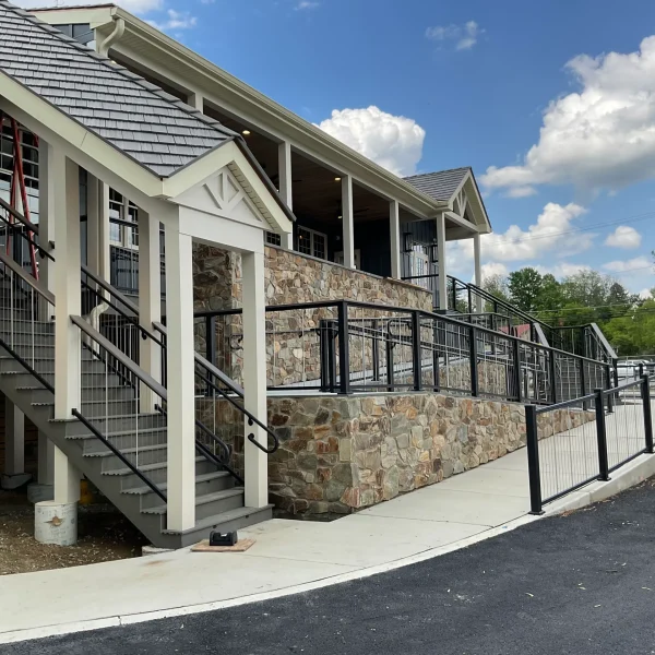 Stone-clad building exterior with gray stairs and black railings leading to a covered porch under a pitched roof.