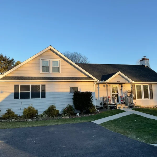 Front view of a beige suburban house with a gabled roof and a yard decorated with Santa figures; clear blue sky.