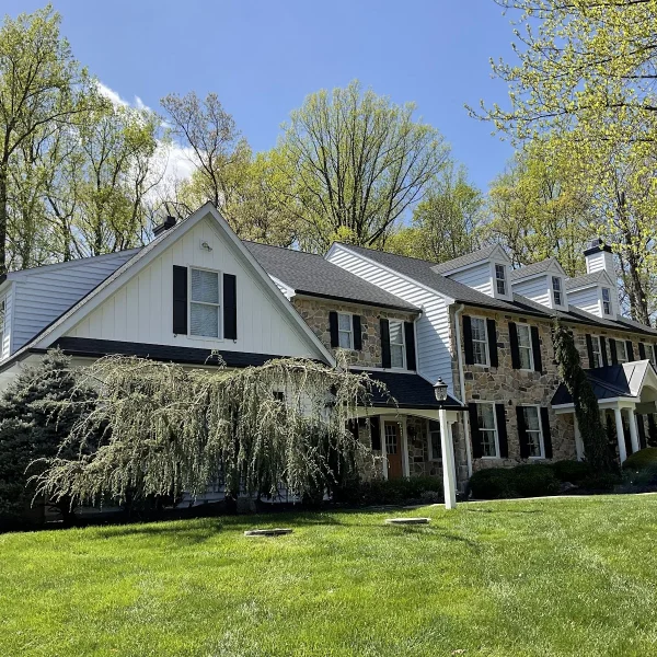 A two-story stone house with fresh white siding completed by an exterior remodeler in Radnor Township, PA.
