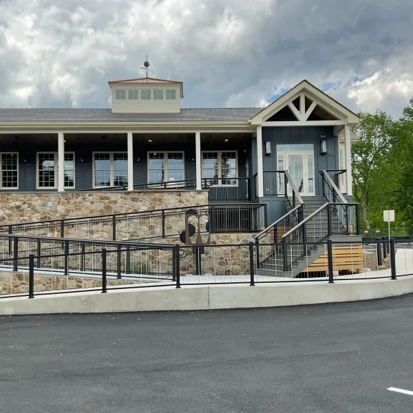 Blue storefront with stone base and white trim, covered porch, railings, and a red ladder against the wall under a cloudy sky.
