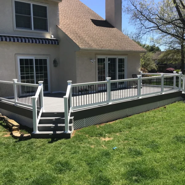 Backyard view of a beige stucco house with a raised white railing deck and sliding glass doors, on a sunny day.