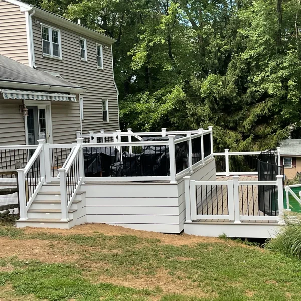 Decked backyard with white railing attached to beige siding house; black furniture covers on the deck, trees in the background.